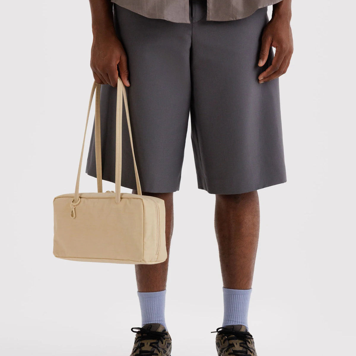 Person wearing gray shorts and holding a beige bag on a white background
