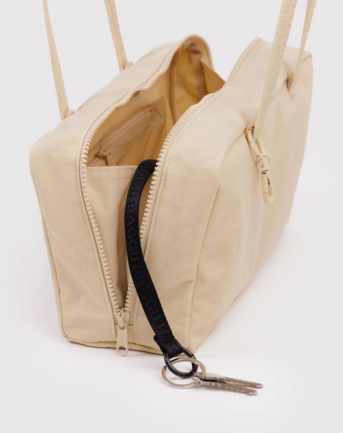 Beige handbag with a black strap and keychain on a white background
