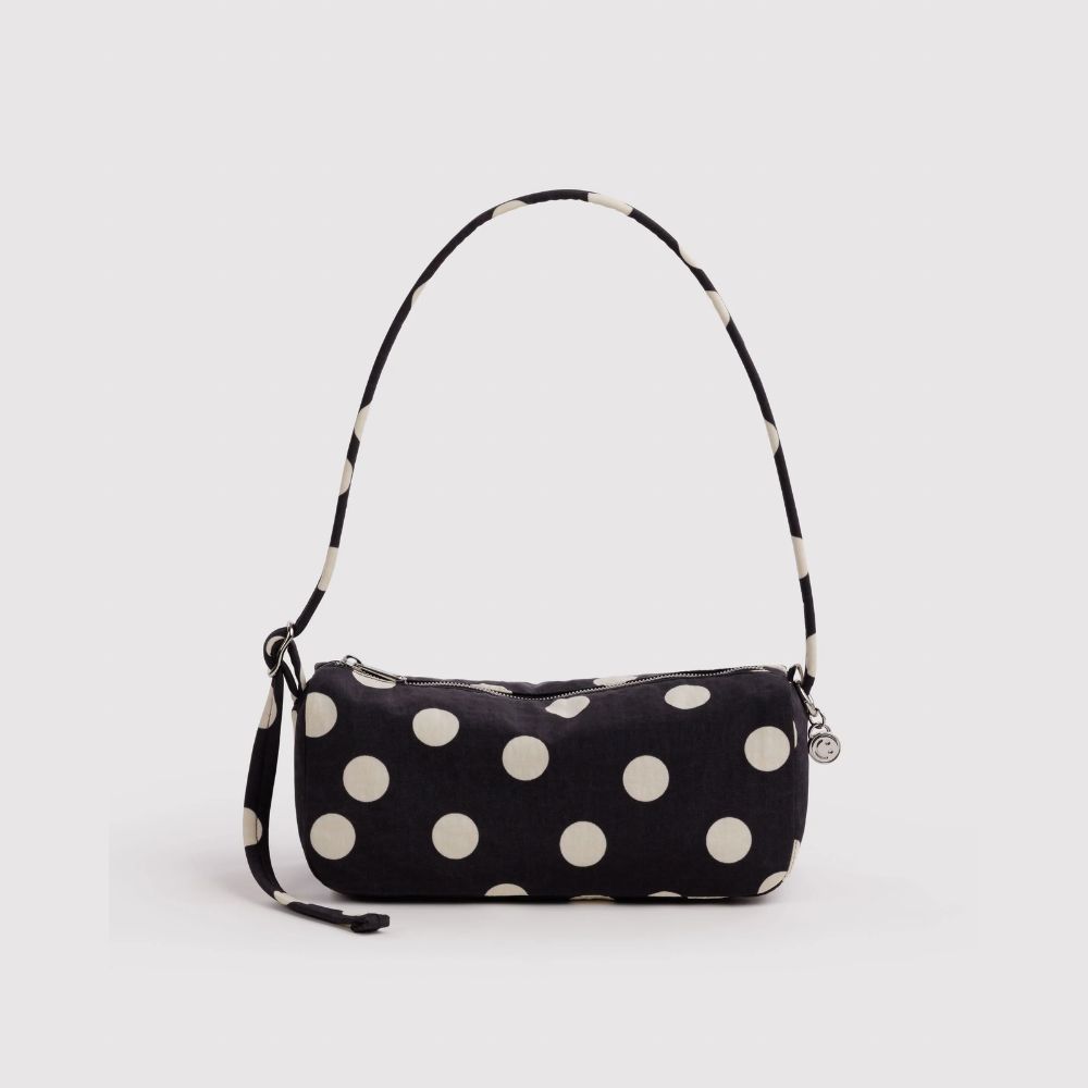 A black fabric shoulder bag with large white polka dots and a matching black-and-white polka dot strap, shown on a light gray background.