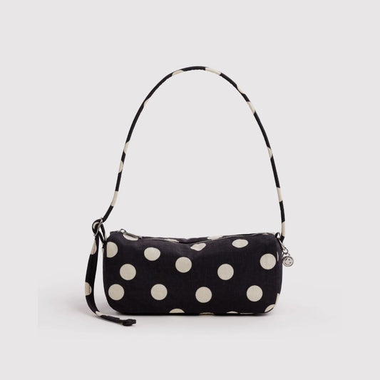 A black fabric shoulder bag with large white polka dots and a matching black-and-white polka dot strap, shown on a light gray background.