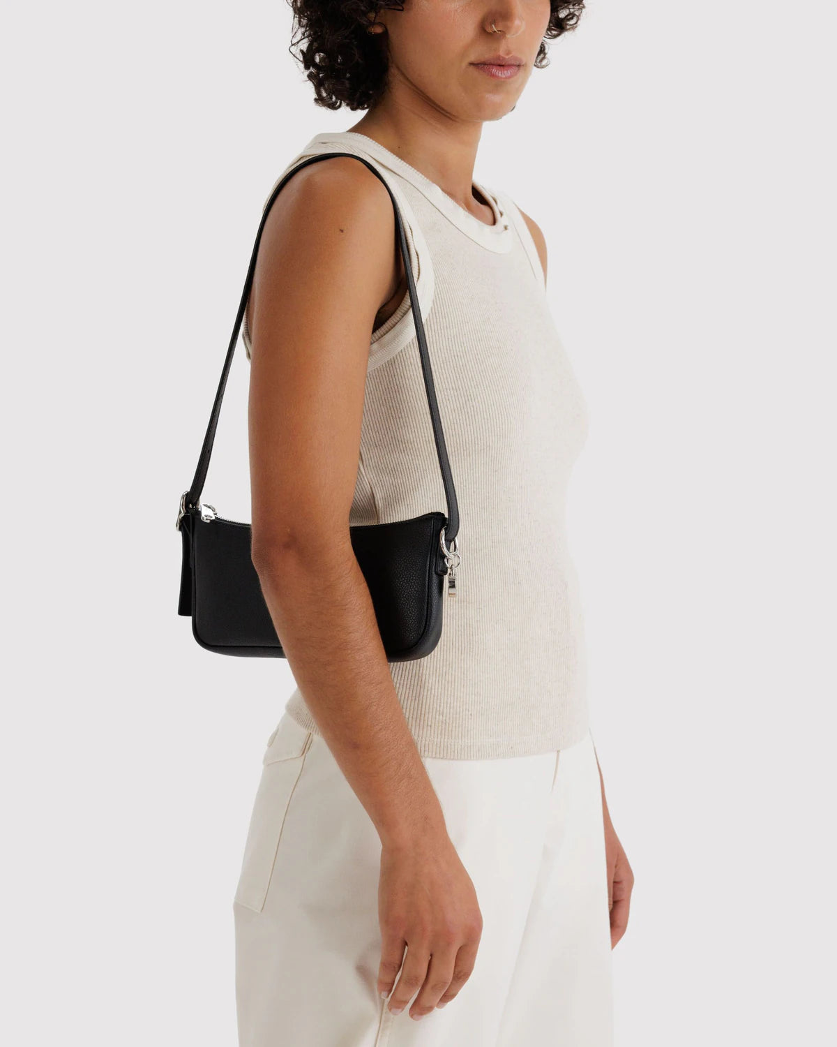 Person wearing a white sleeveless top and holding a black handbag against a white background