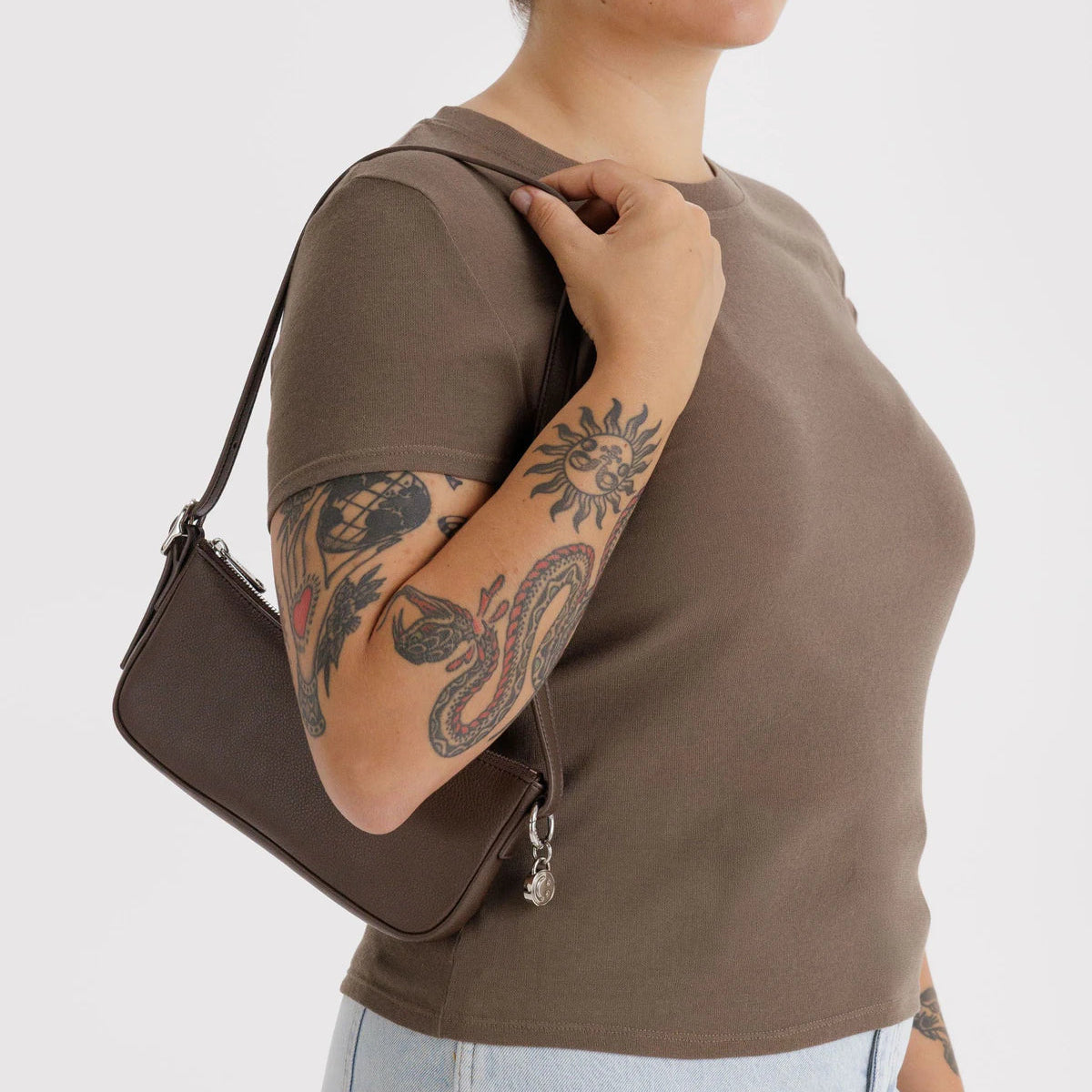 Person wearing a brown shirt and holding a matching brown bag against a white background