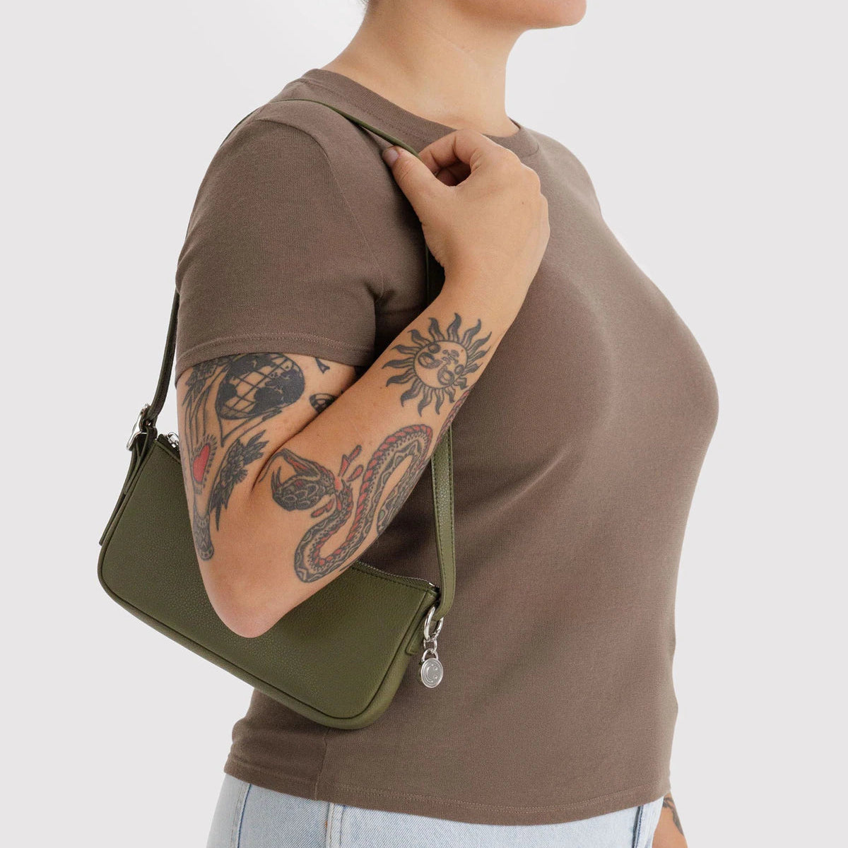 Person wearing a brown shirt and holding a green bag on a light gray background