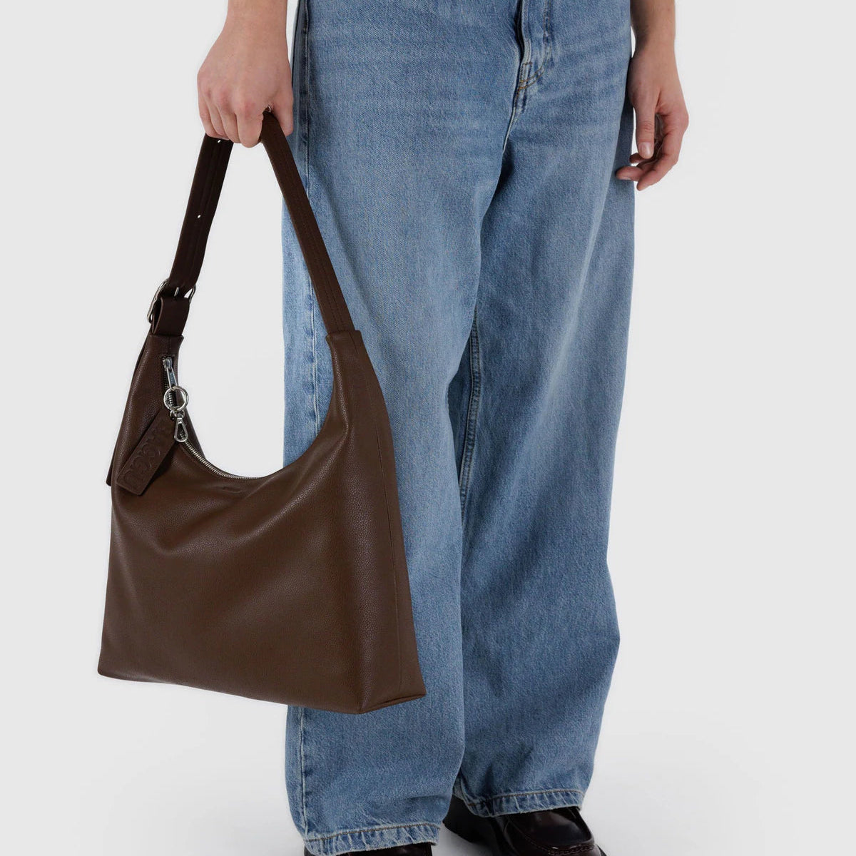 Person holding a brown leather bag wearing blue jeans on a white background