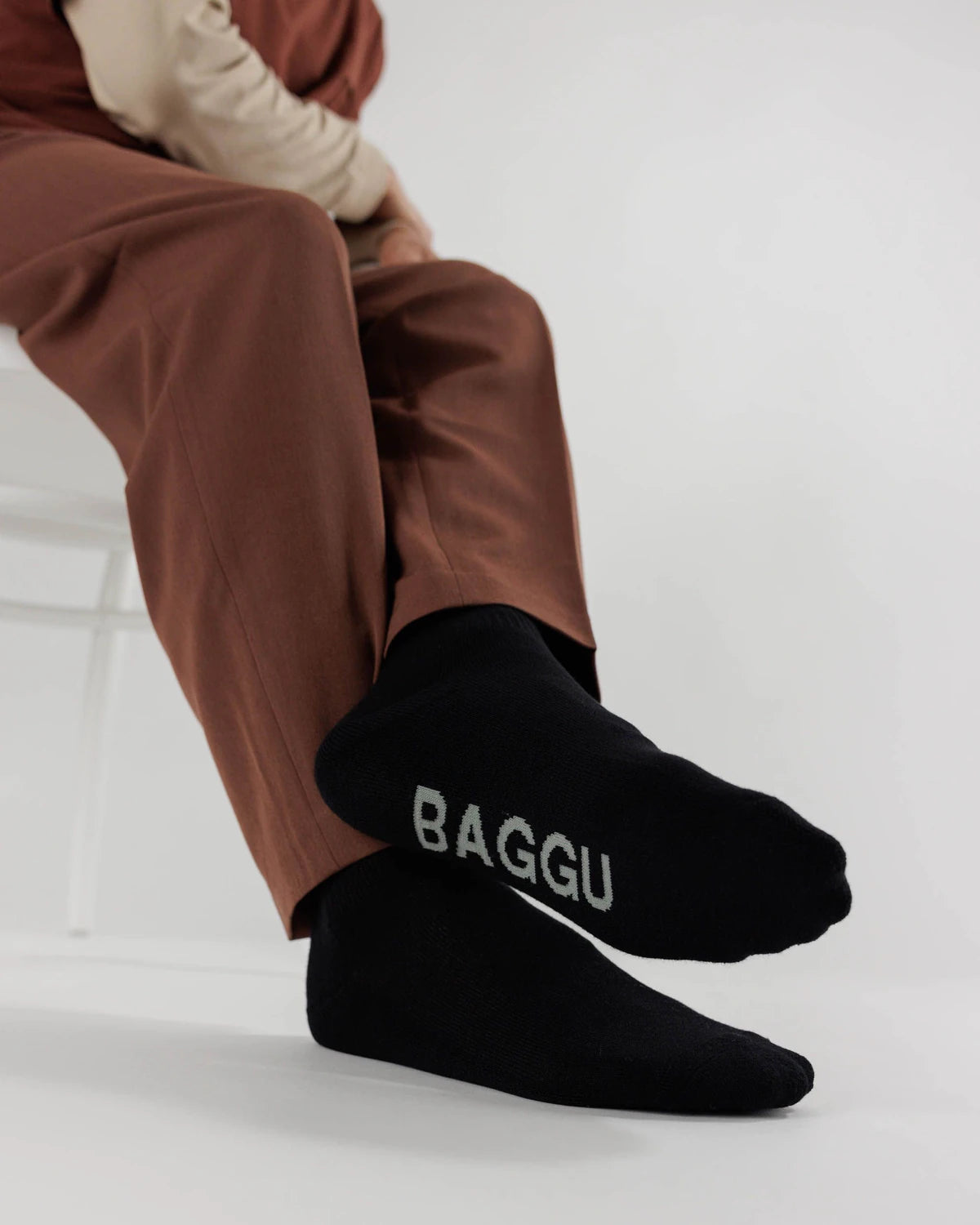 Person wearing brown pants and black socks with 'BAGGU' logo on a white background