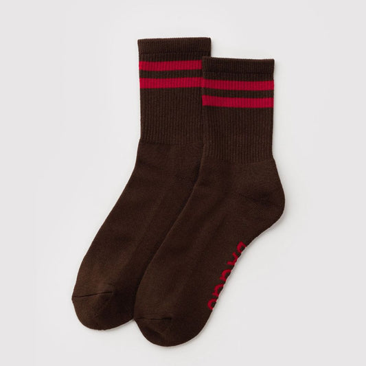 A pair of dark brown crew socks with two red stripes near the ribbed cuffs and red text branding on the sole, displayed on a light gray background.