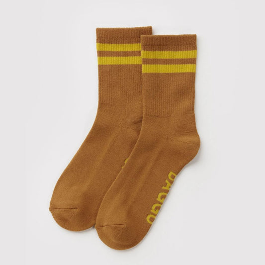 A pair of brown crew socks with two yellow stripes near the cuff and yellow branding printed on the sole, displayed on a light gray background.