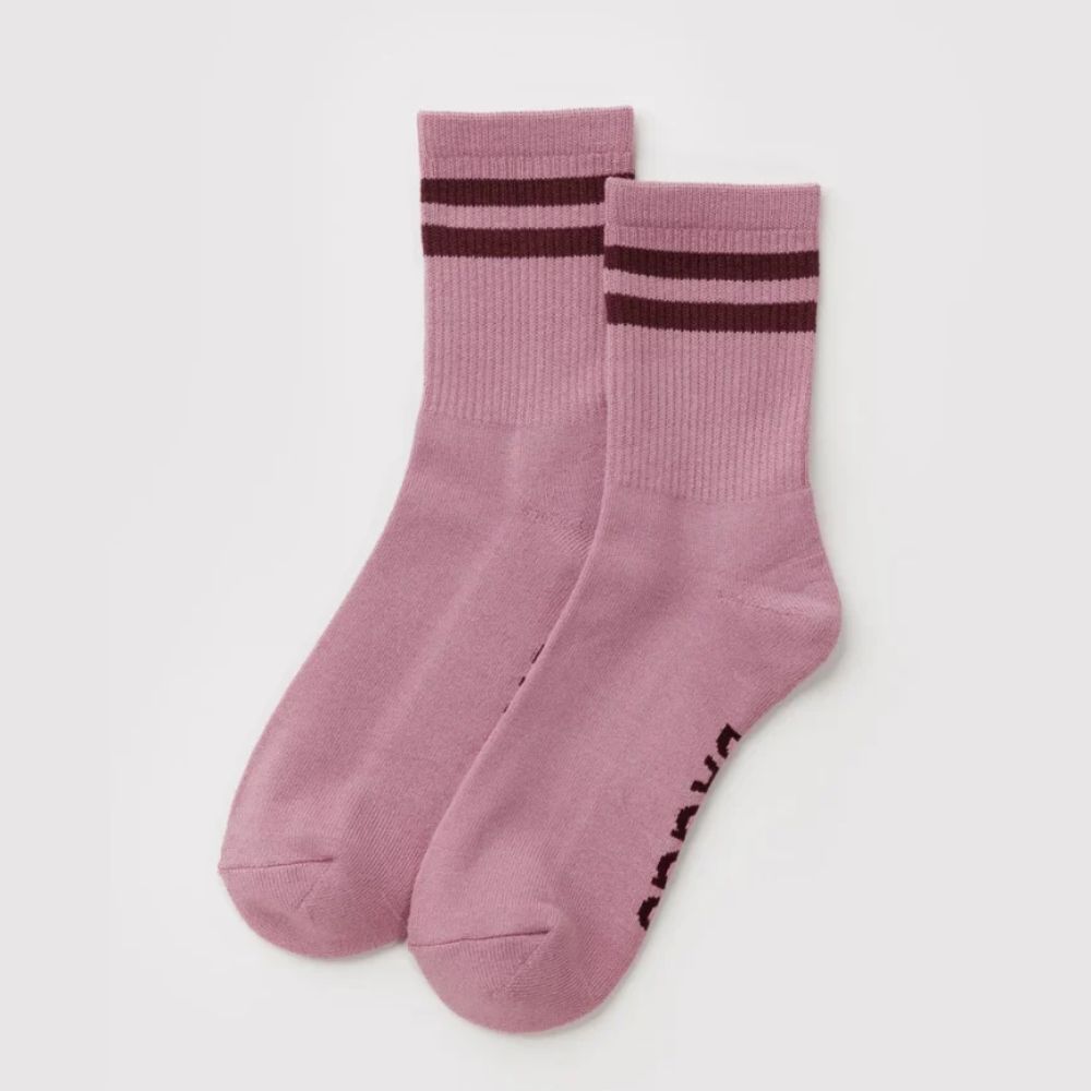 A pair of dusty pink crew socks with dark brown stripes near the cuff and dark brown text on the sole, displayed on a light gray background.