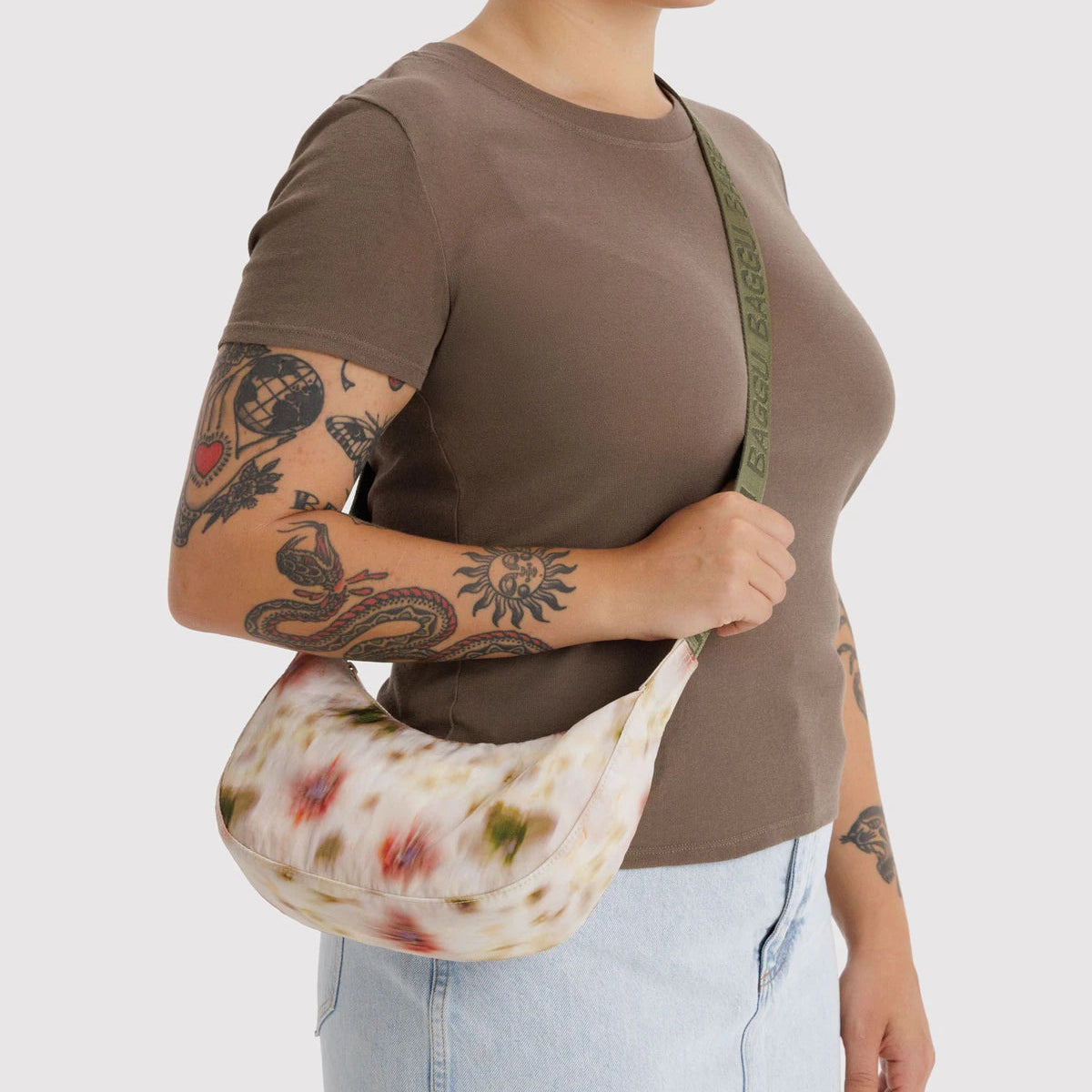 Person wearing a brown shirt and light blue jeans, holding a floral-patterned bag against a white background