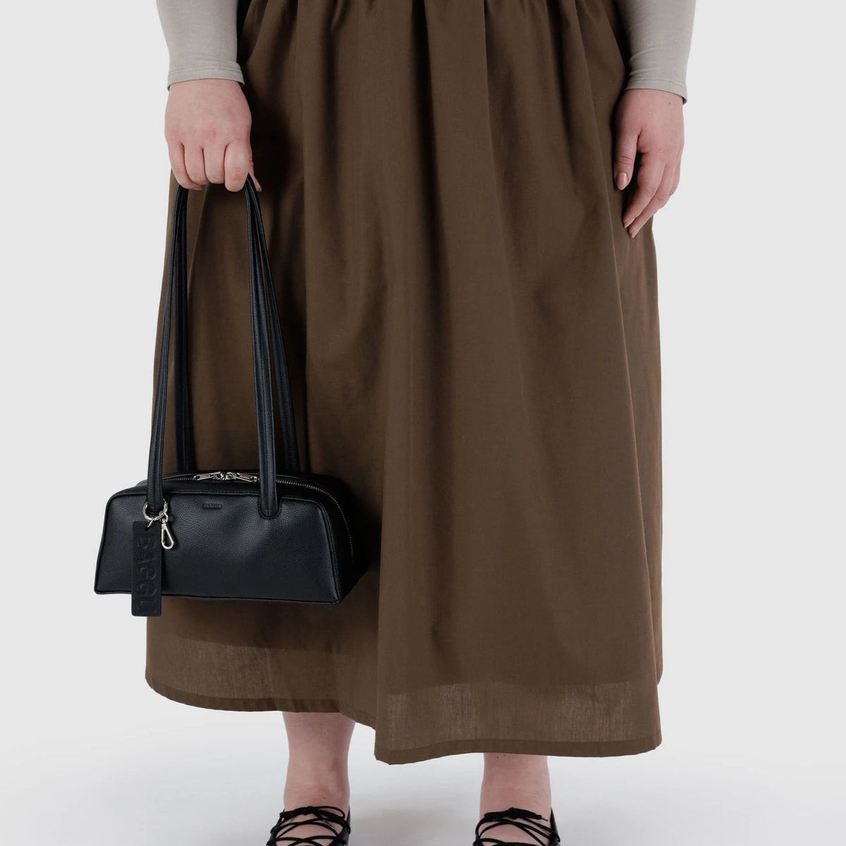 Person wearing a brown skirt holding a black handbag on a white background