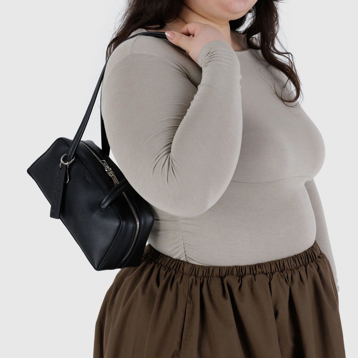 Person wearing a gray long-sleeve top and brown skirt with a black handbag on a white background