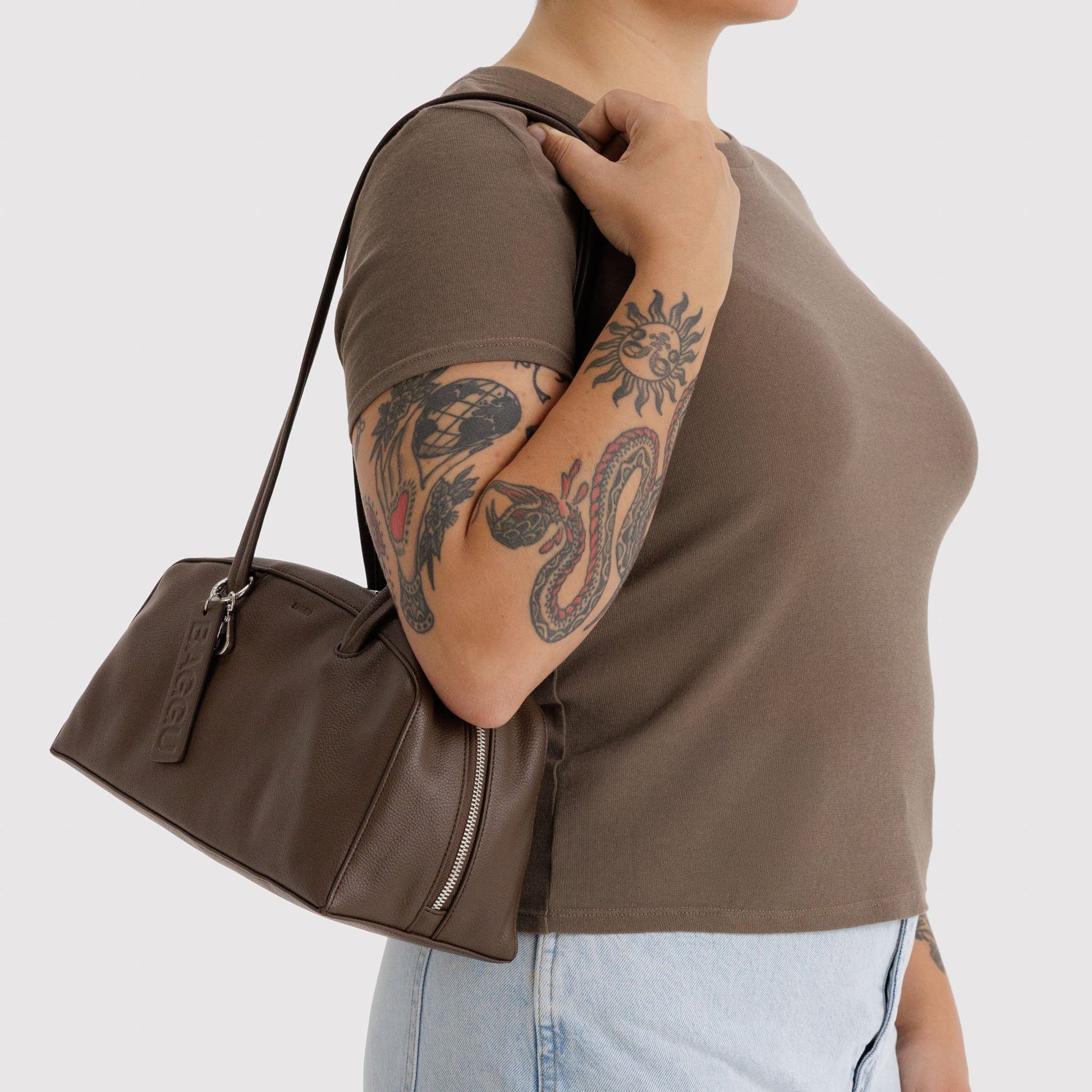 Person wearing a brown leather handbag on a plain background
