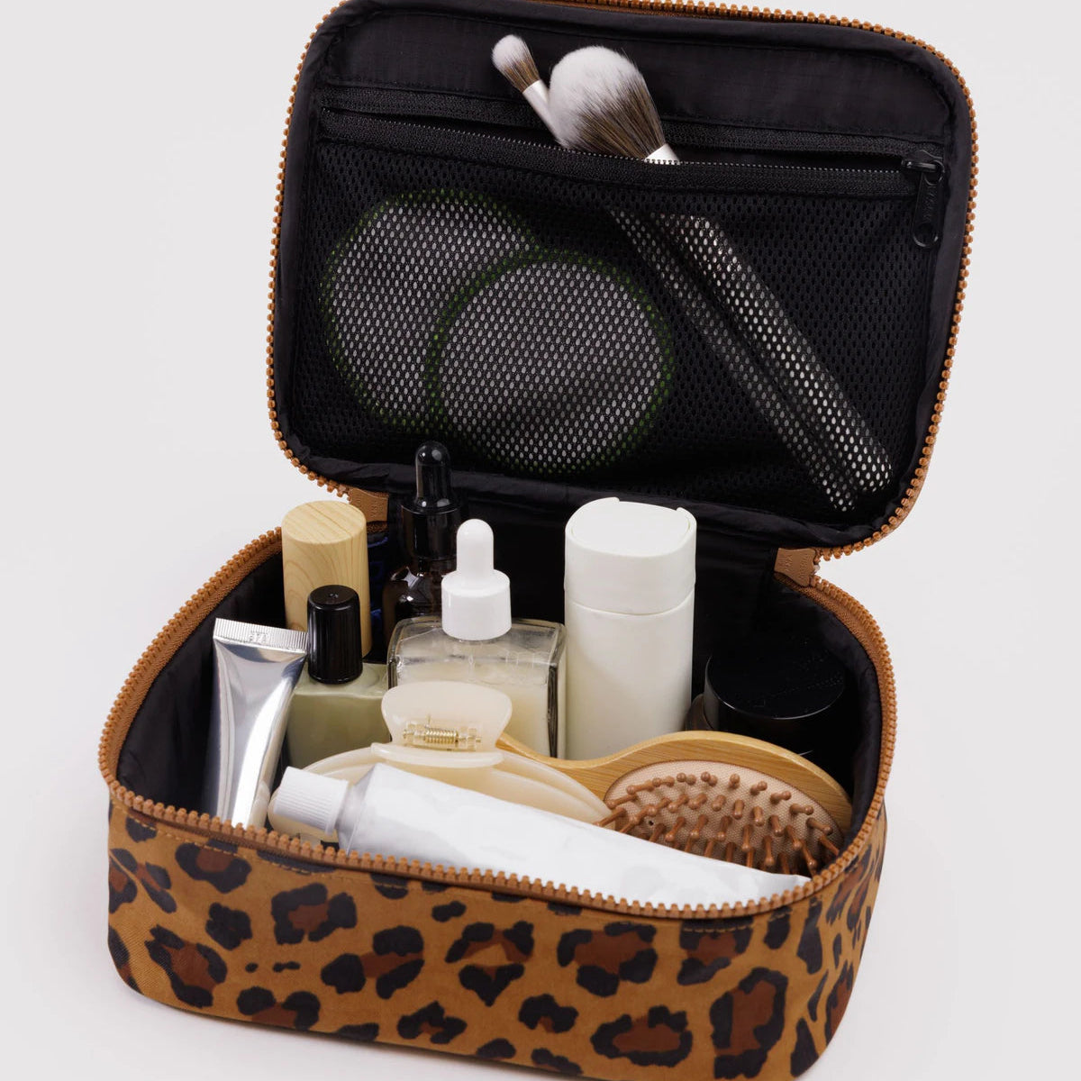 Makeup case with leopard print exterior, containing various cosmetic items on a light gray background