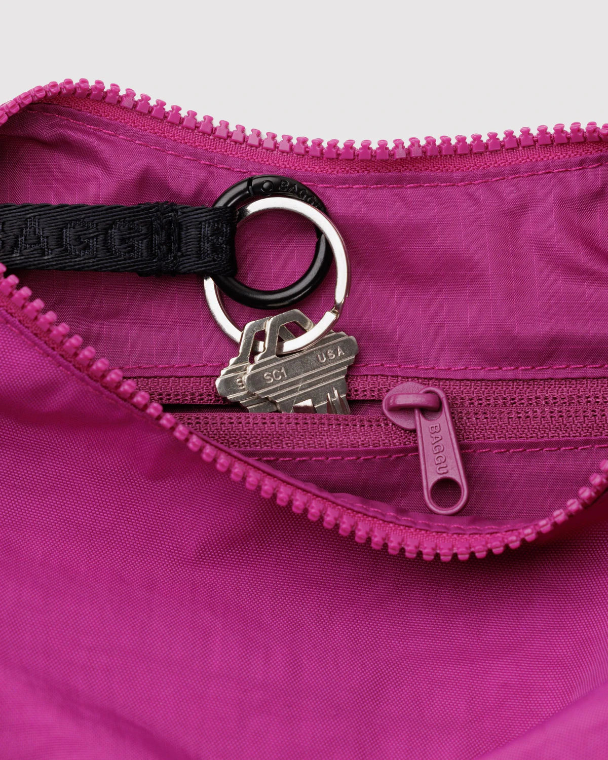 Close-up of a pink bag with a black strap and silver keychain on a light gray background