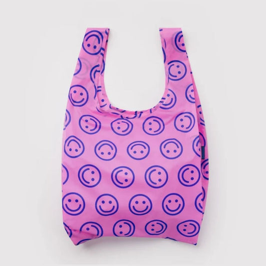 A reusable plastic bag with a pink background and a repeating pattern of dark purple smiley faces, shown against a plain light gray background.