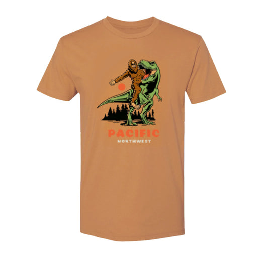 Light Brown tshirt with a sasquatch riding a t-rex. Text underneath image on shirt reads Pacific Northwest