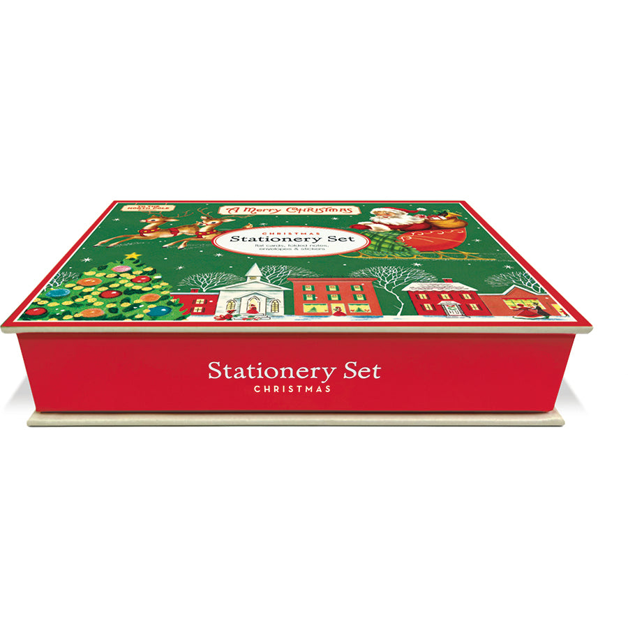 A Christmas-themed stationery set in a red box with a festive illustrated lid showing Santa, reindeer, a Christmas tree, and holiday buildings. The front of the box reads 'Stationery Set Christmas'.