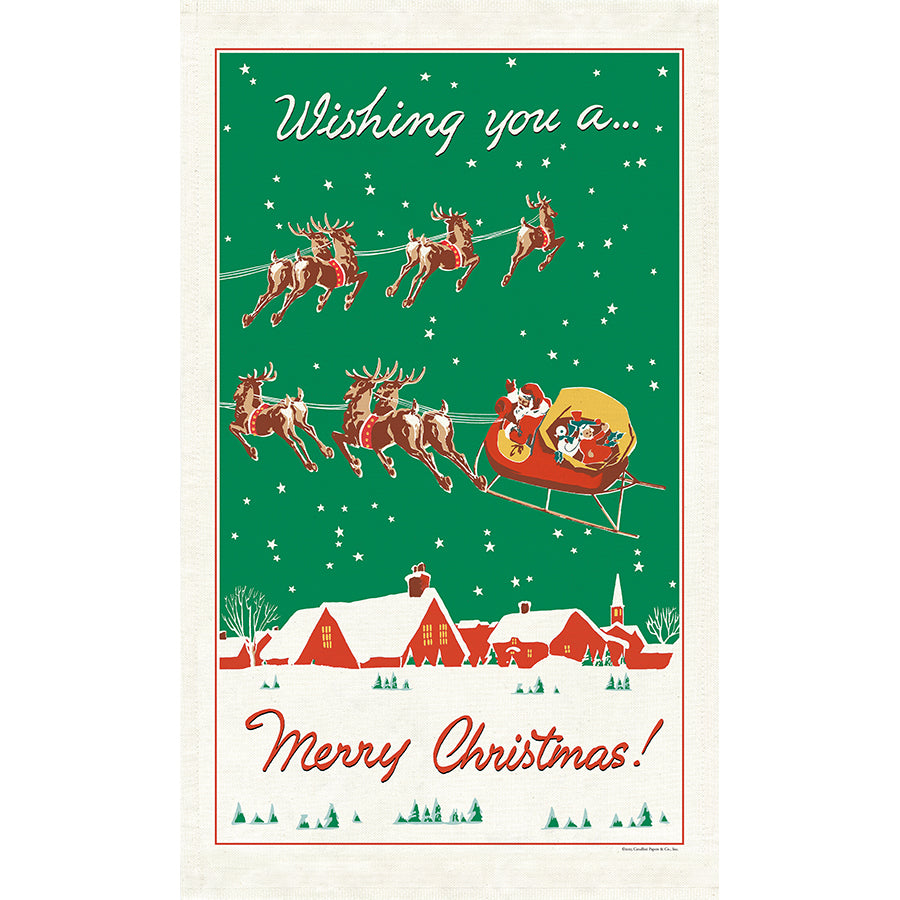 A festive Christmas-themed tea towel with a cream border, featuring Santa Claus in a sleigh carrying a sack of gifts against a green starry sky, with reindeer flying above snowy red-roofed houses. 