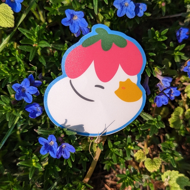Illustrated duck sticker with little flower hat nestled in grass with blue flowers