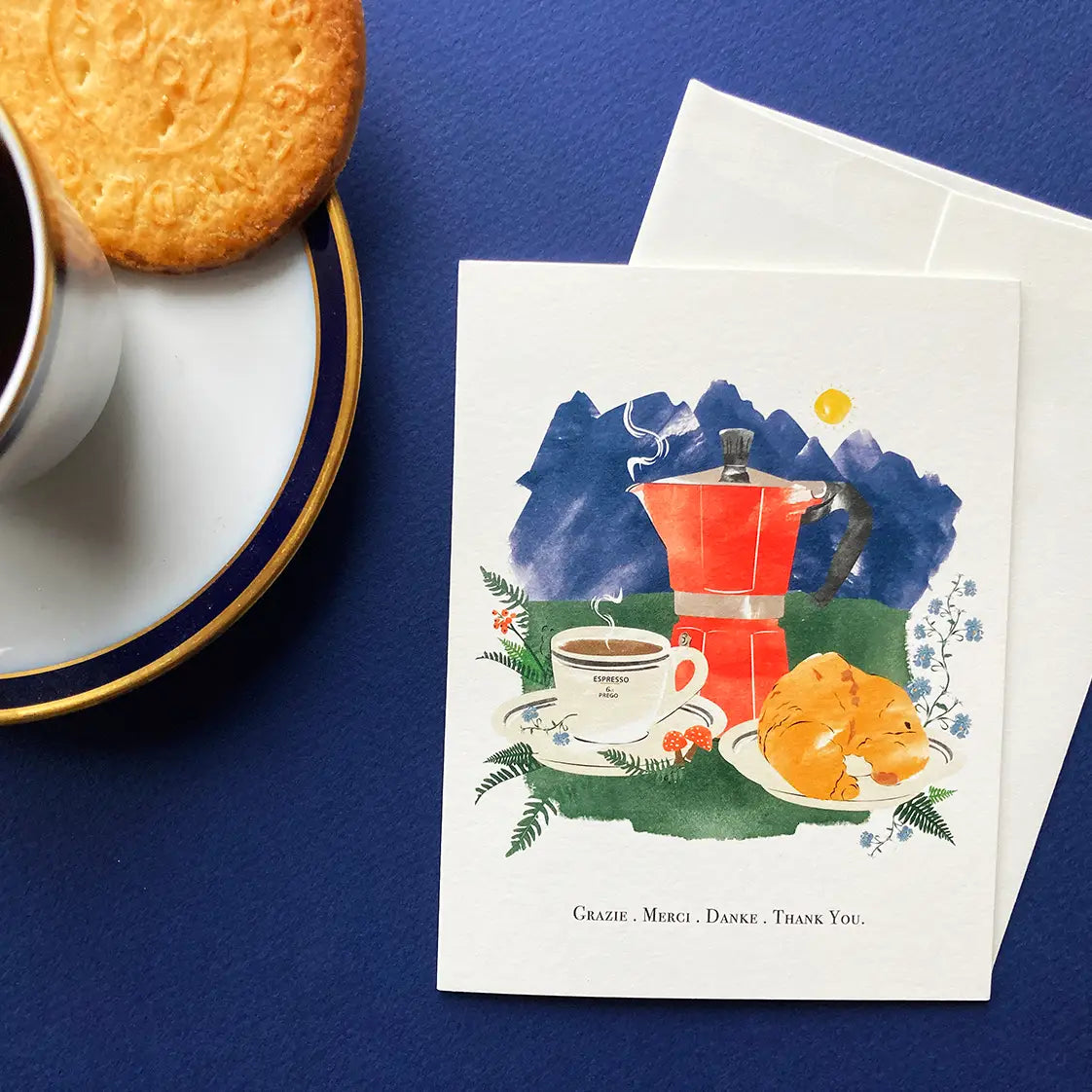 Greeting card with coffee-themed illustration on a blue surface with a cup of coffee and cookie.