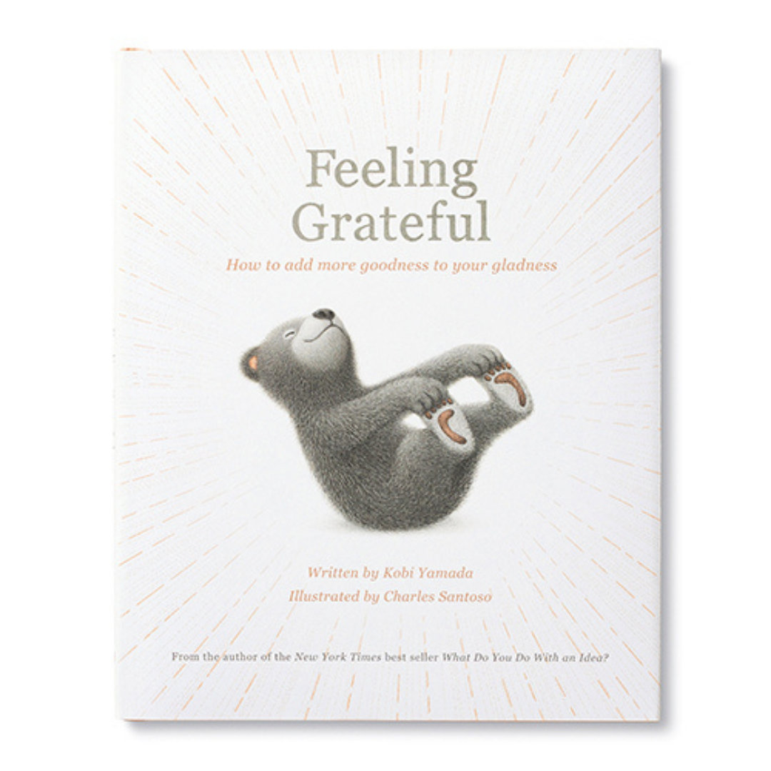 Cover of "Feeling Grateful- How to add more goodness to your gladness" Written by Kobi Yamada Illustrated by Charles Santoso From the author of the New York TImes best seller "What Do You DO With an Idea?"
At the center of the cover is a smiling bear cub holding onto their toes and rocking back, ray-like lines radiate from the bear to the edges of the cover.