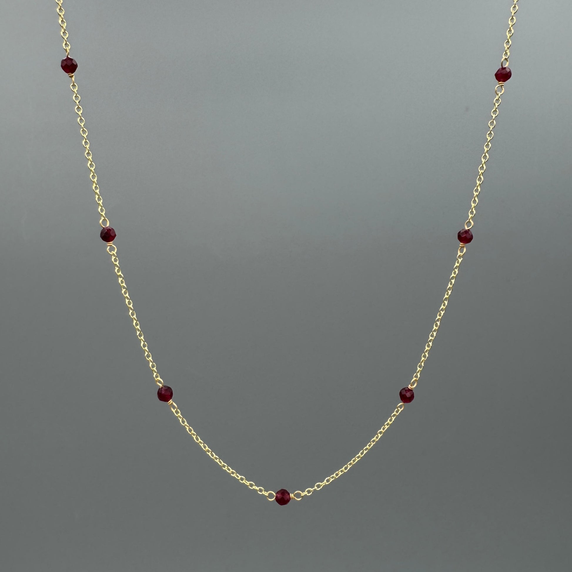 Gold necklace with dyed red beads on a gray background
