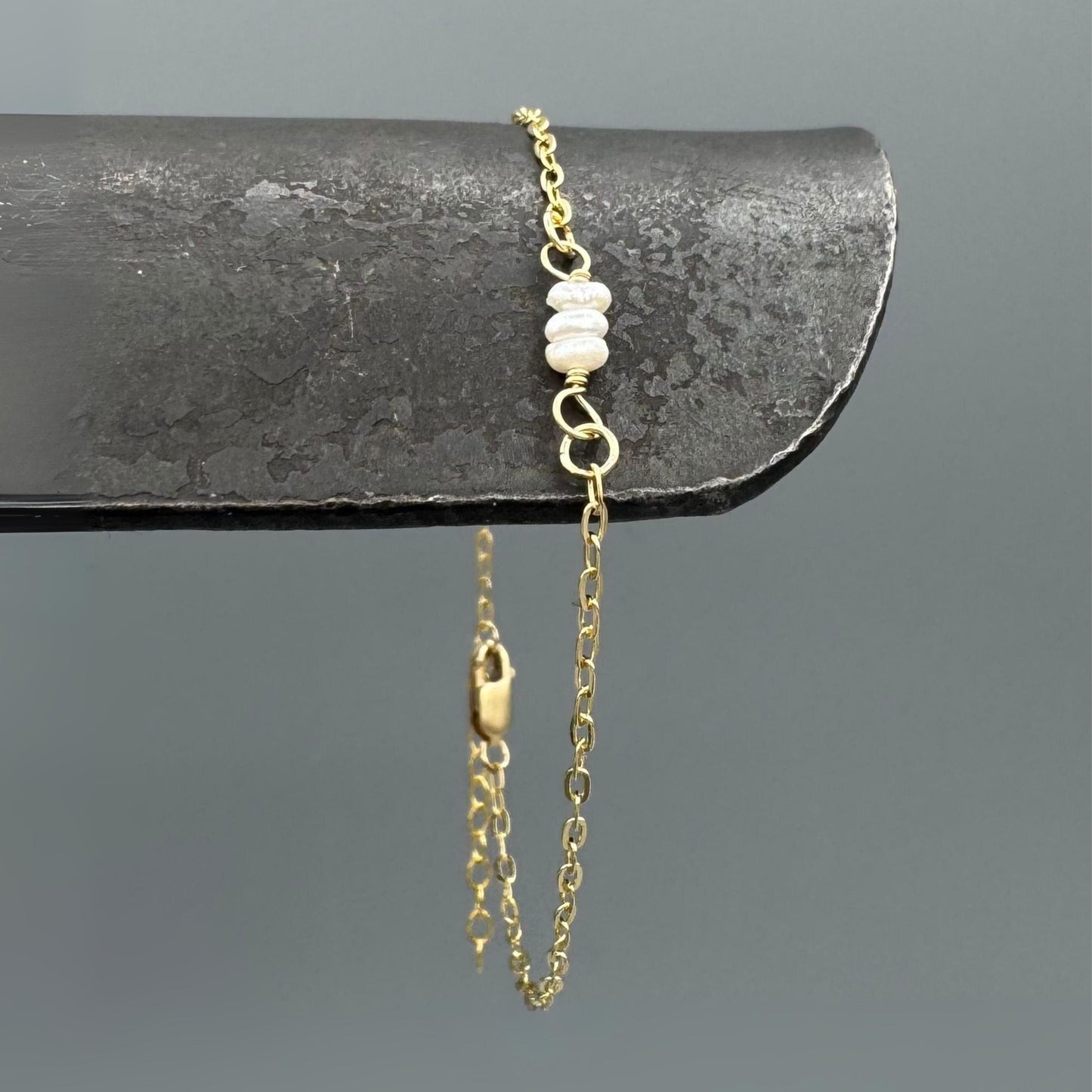 Gold chain bracelet with pearl beads on a dark surface