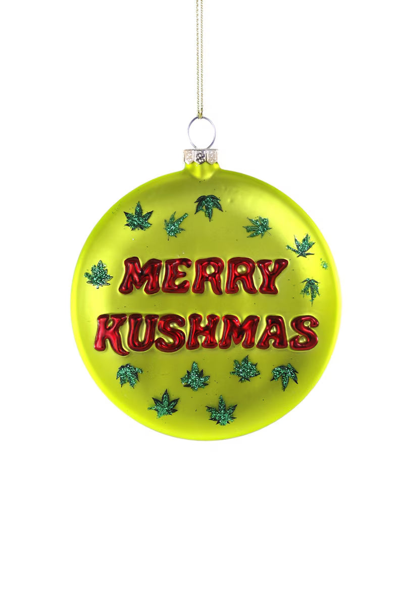 Green glass ornament says "Merry Kushmas" in red and is decorated with green glitter pot leaves.