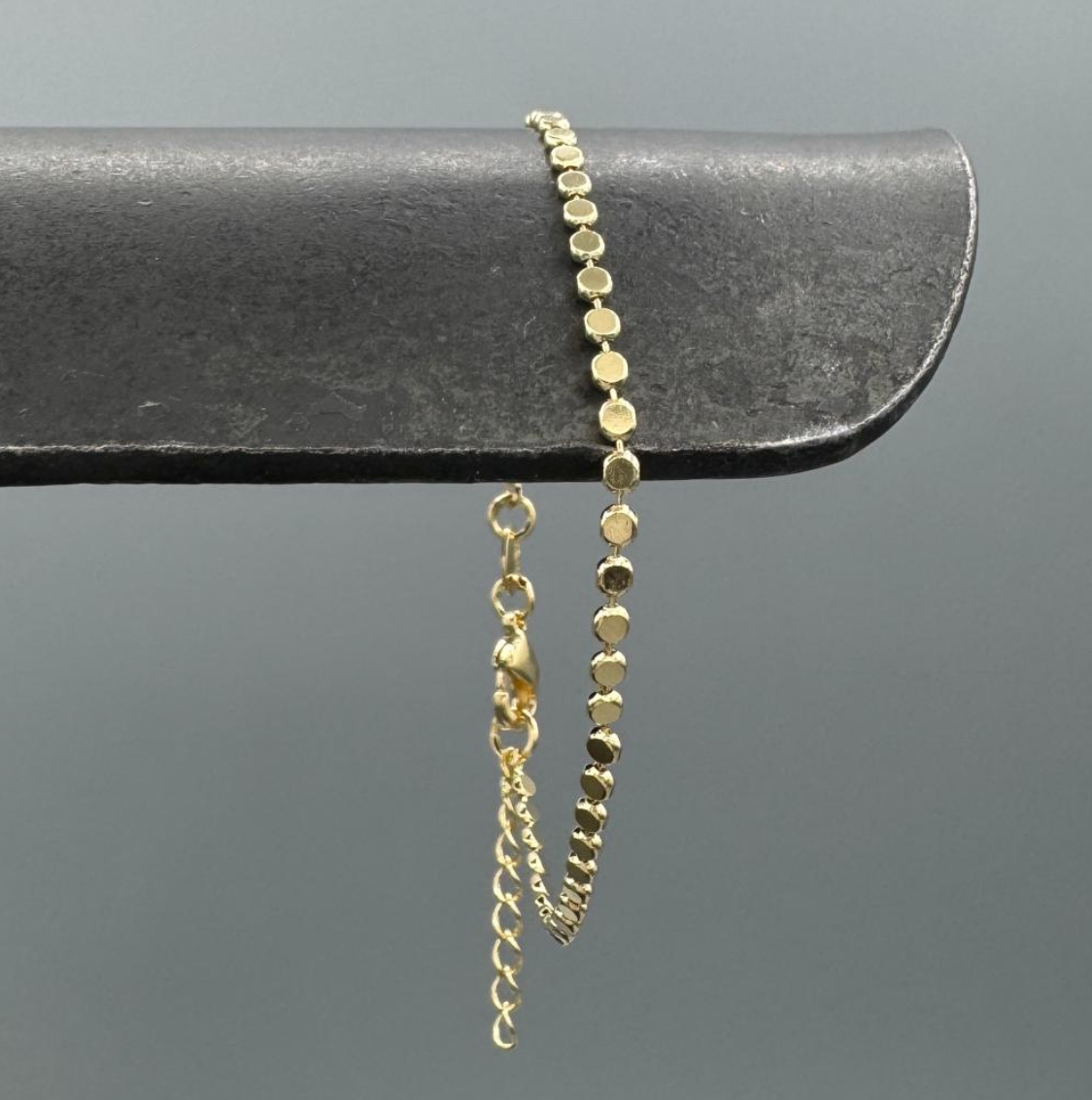 Gold bracelet with a chain extension on a gray background