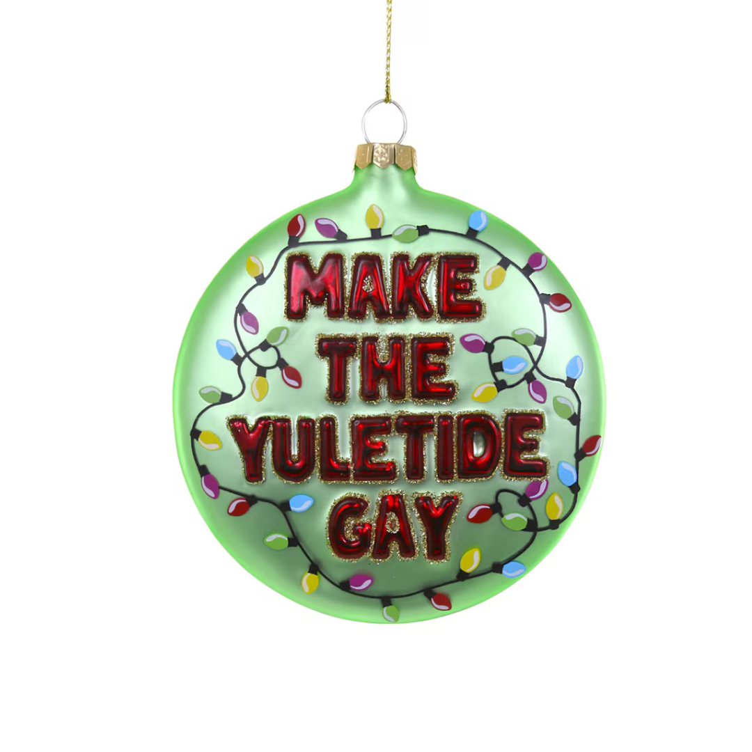 Green glass holiday ornament decorated with rainbow twinkle lights that says "Make the Yuletide Gay" in red