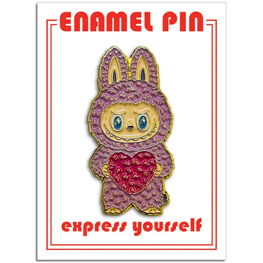 Enamel pin with cartoon character in a purple hood holding a pink heart, on a white background with red text.