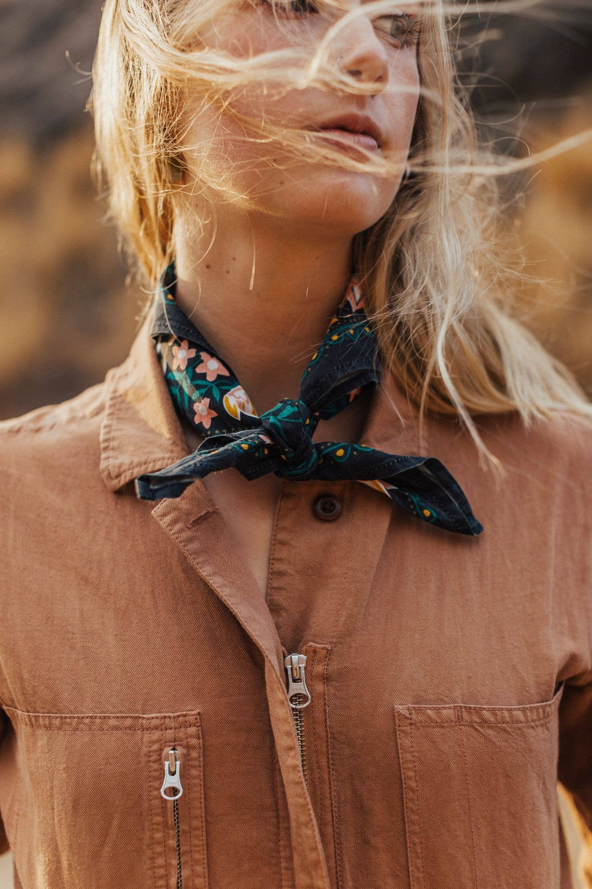 Person wearing a brown jacket with a floral scarf around their neck, outdoors.