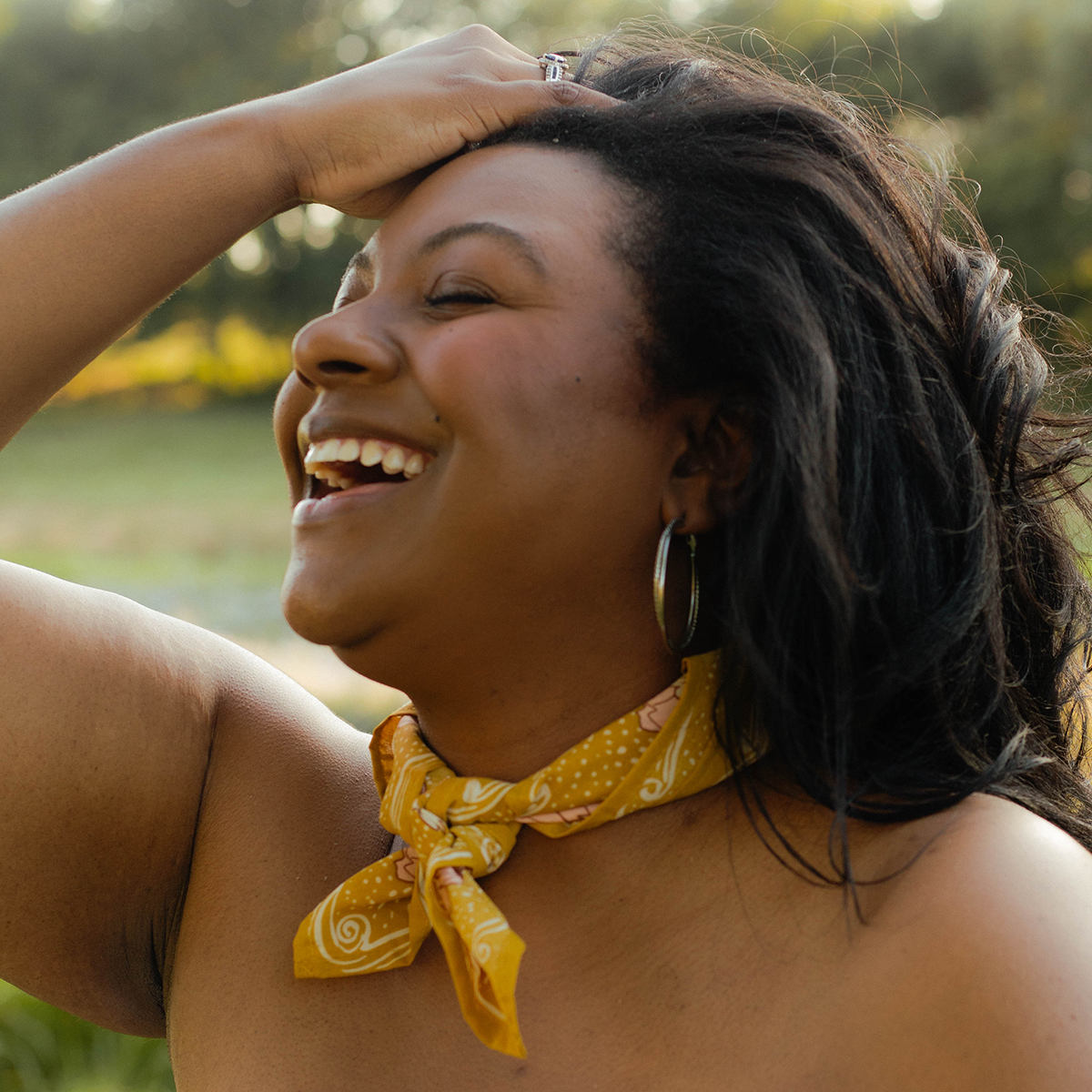 Woman laughing outdoors with a yellow bandana around her neck