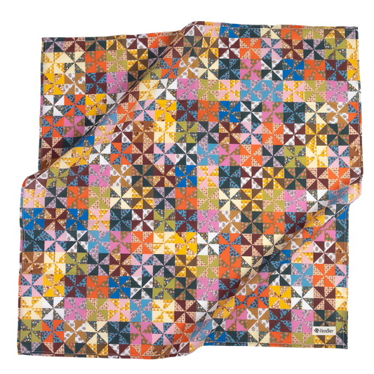 A square scarf featuring a colorful geometric patchwork pattern of triangles and squares in many shades, including pink, blue, yellow, orange, brown, green, and white. 