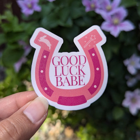 Sticker featuring pink horseshoe with the words "good luck babe" inside.