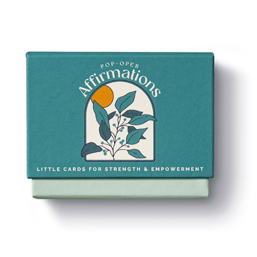 Box for "Pop-Open Affirmations- Little Cards for Strength & Empowerment" 
Box is deep green and features an illustration of a branch of leaves and an orange sun in a cream colored arch.