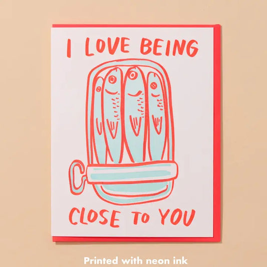 Card with illustration off four fish in a tin and text 'I love being close to you' on a beige background.