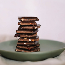 Load image into Gallery viewer, Pieces of chocolate bar stacked in a tower on a green plate.

