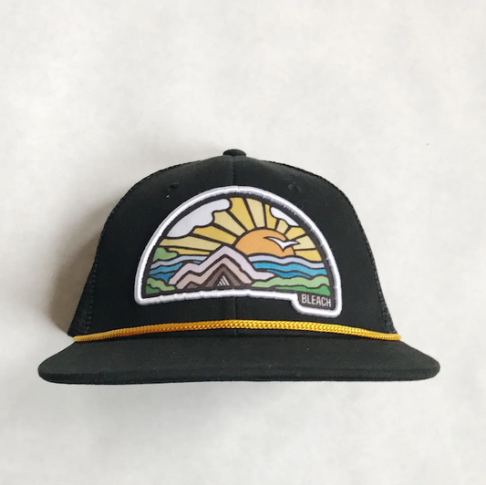 Black hat with patch detail of sunrise over a mountain on a while background.
