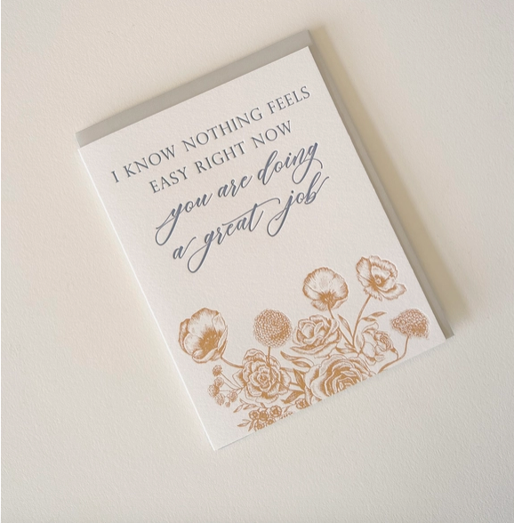 White card with orange illustrated flowers on bottom and blue text saying "I know nothing feels easy right now, you are doing a great job"