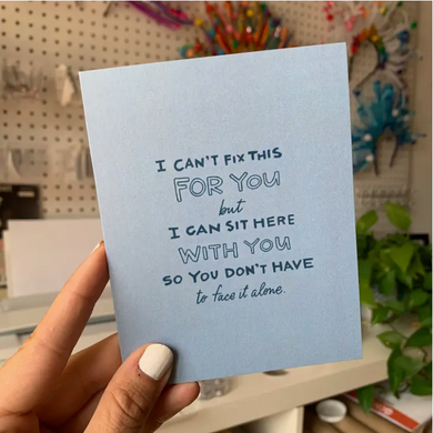 Hand holding blue card in front of bright background. Text in blue reads 