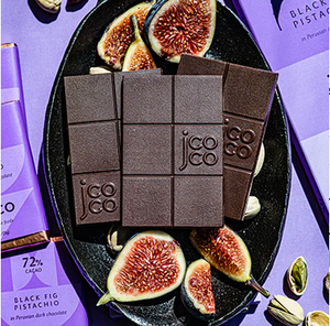 Chocolate bars nestled on a plate with figs and pistachios on a purple background.