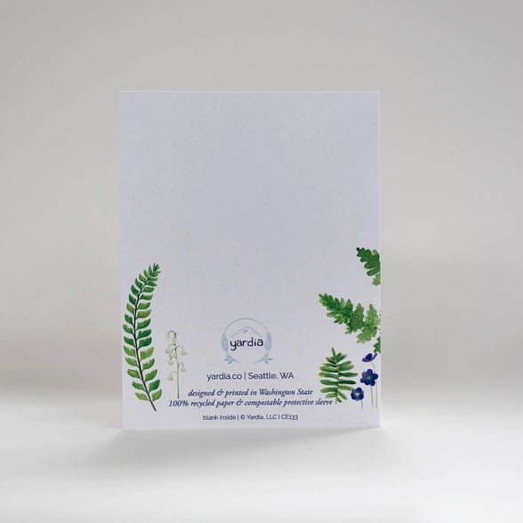 Back of white card on white background. Card has small ferns and circular Yardia Logo