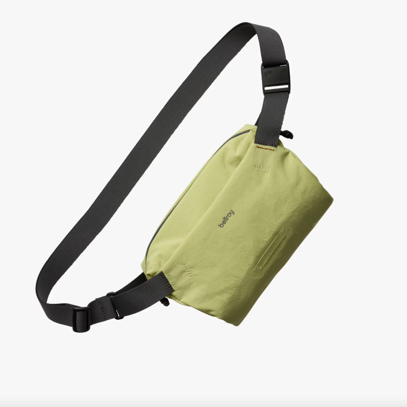 Green sling bag with black strap on a white background.