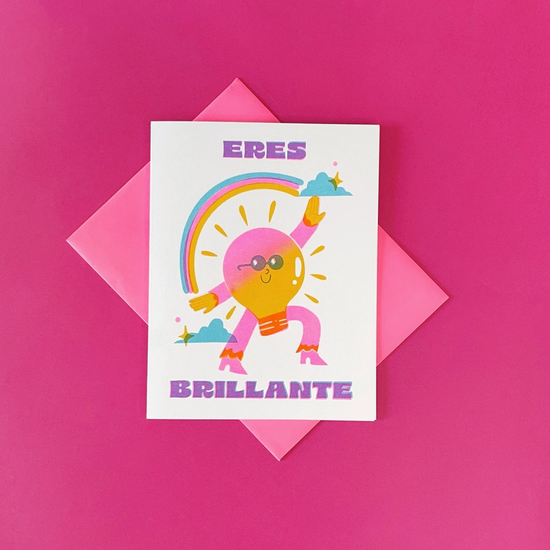 White card on pink background featuring a cartoon rainbow and lightbulb. Text reads in Spanish "Eres Brillante"