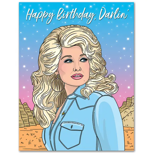 Greeting card featuring illustrated drawing of Dolly Parton in front of a desert sunset landscape. White cursive text on top of the card says "Happy Birthday, Darlin'"