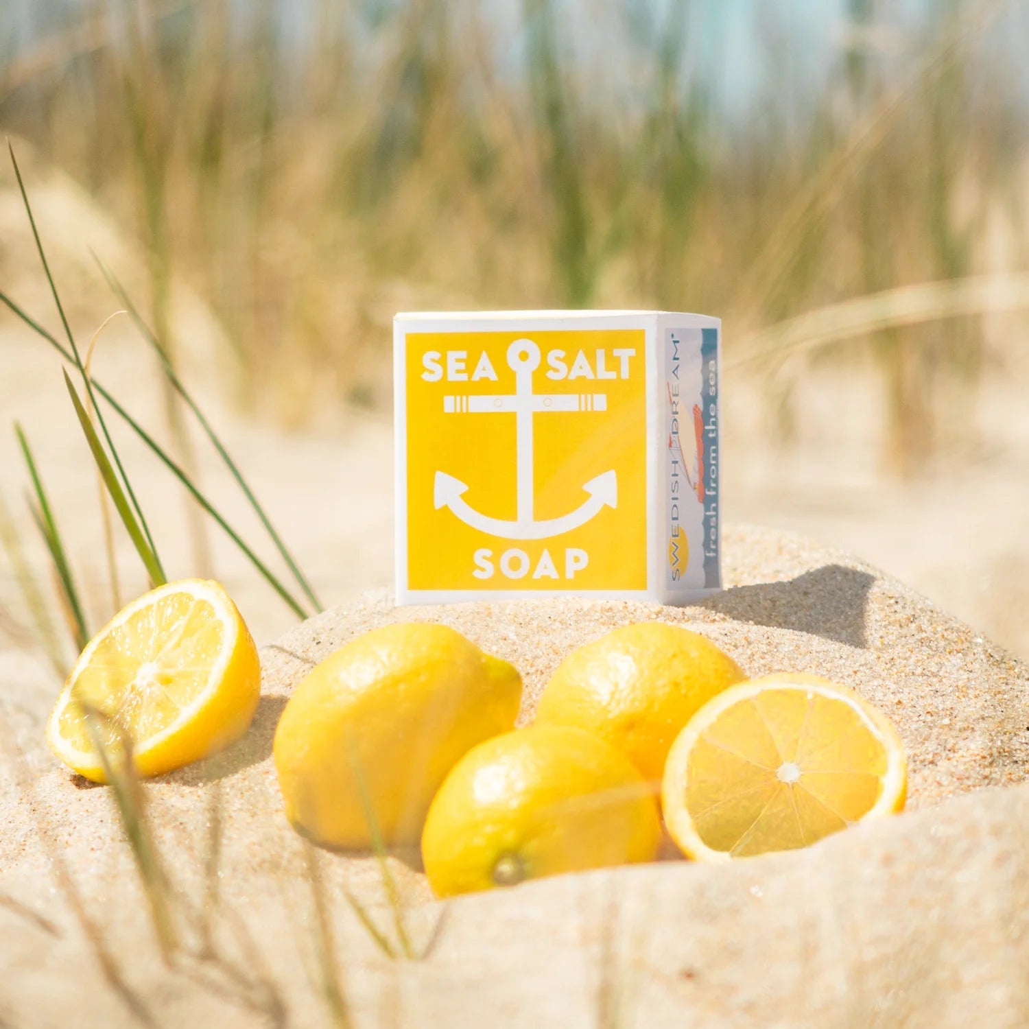 Sea Salt Lemon soap packaging on a sandy beach with a pile of fresh lemons.