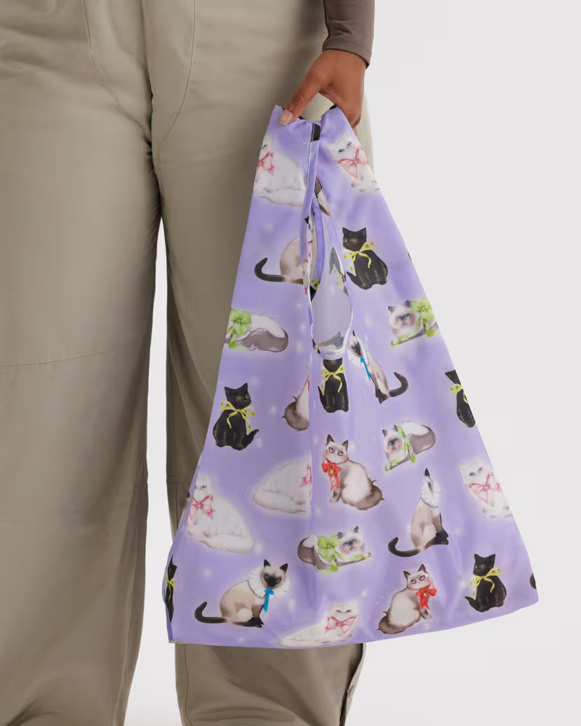 Person holding a purple reusable bag with cat patterns on a plain background