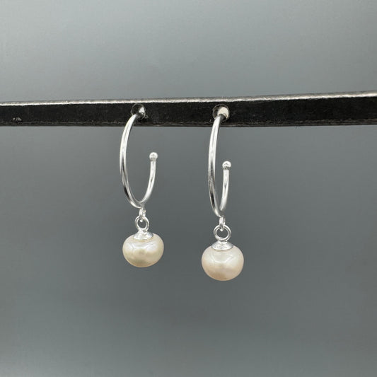 Silver hoop earrings with pearl drops on a gray background