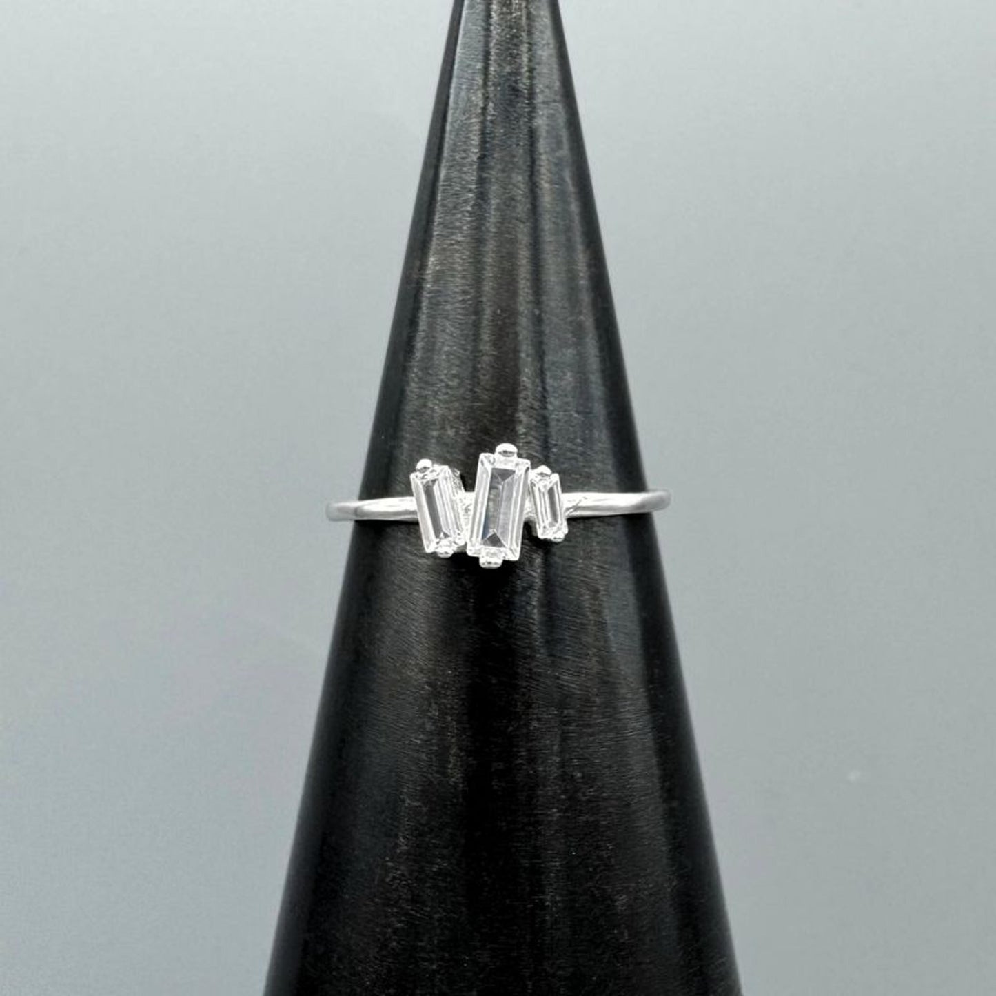 Silver ring with baguette-cut gemstones on a black stand against a gray background